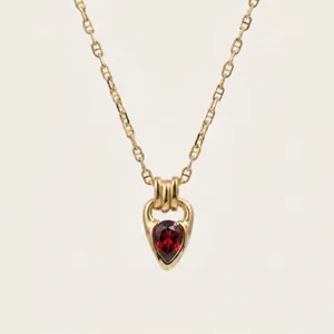 Detail view of a teardrop red zircon necklace with 18K gold plating and horseshoe clasp