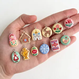 Variety of folk art ceramic charms with Matryoshka and floral prints held in hand.
