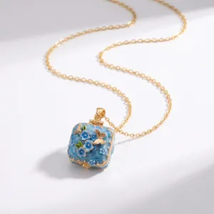 Detailopname van een vierkant emaille medaillon met blauwe bloemen- en vlindermotieven.