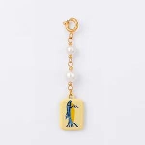 Detail view of marine life pearl charm with fish illustration on yellow ceramic tile