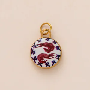 Close-up of a circular gold-rimmed pendant featuring red prawn illustrations on white background.