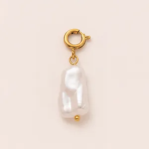 Detail of large baroque pearl pendant with golden circular clasp on beige background.