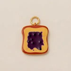 Detailweergave van een acryl bedeltje in toastvorm met paarse jam en gouden ring.