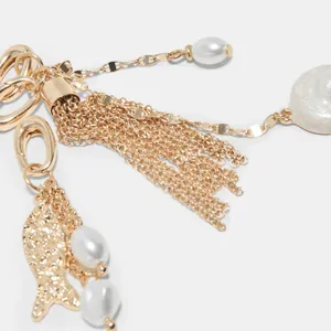 Makroansicht des goldenen Bikini-Anhängers mit Perlen und Fischquasten-Detail.