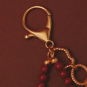 Primo piano del moschettone dorato e delle perle rosse su un ciondolo per borsa in stile cinese.