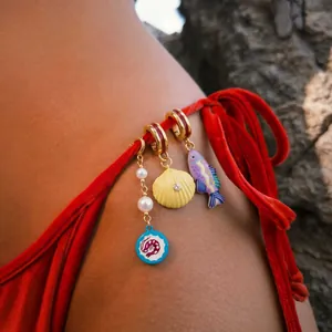 Dettaglio di ciondoli marini su un laccetto di bikini in velluto rosso per l'estate