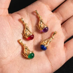 Macro view of four Egyptian Bastet cat pendants with colorful gemstones on a hand.