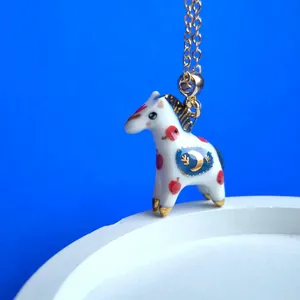 Inquadratura dettagliata del ciondolo cavallo in ceramica con catena dorata e luna