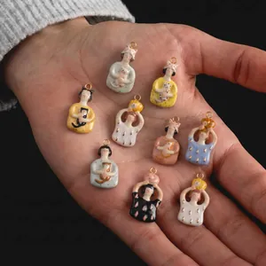 Detailed view of handmade ceramic girl and cat charms held in a palm for DIY crafts