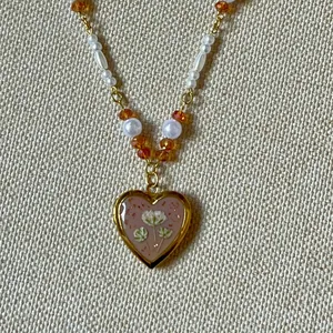 Close-up of a vintage heart locket necklace with floral pattern and pearl beads.