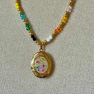 Close-up of a vintage gold locket necklace with colorful dried flowers and beads