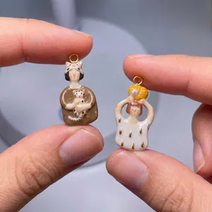 Close-up detail of hand-painted ceramic girl and cat charms for DIY jewelry making