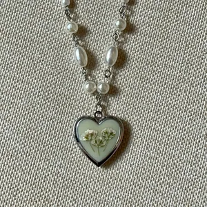 Close-up of a vintage heart-shaped floral locket necklace with elegant pearl chain detail