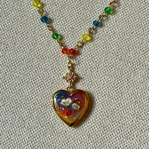 Close-up of vintage heart locket necklace with colorful floral painting and beads