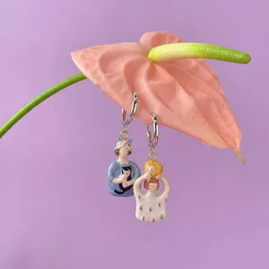 Detailed close-up of cute ceramic girl and cat charms hanging on a pink flower petal