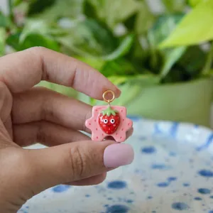 Close-up macro view of a cute pink cartoon strawberry puzzle charm held by a manicured hand