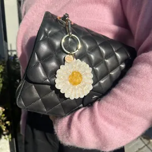 White daisy acrylic bag charm pendant on a quilted black handbag detail