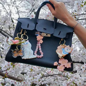 Cute acrylic bag charms with cat and cherry blossom designs displayed on a black handbag