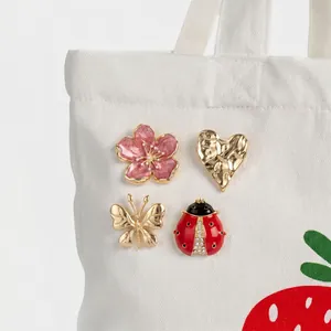 Primo piano di spille in smalto con disegni di coccinella e fiori su una borsa