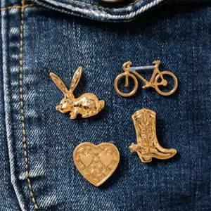 Gros plan de quatre broches vintage dorées : lapin, vélo, botte et cœur sur tissu denim.