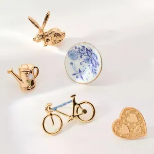 Détail de broches vintage dorées avec motifs de lapin, de vélo et d'assiette fleurie
