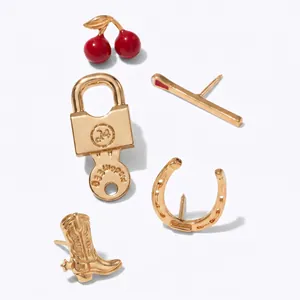 Gros plan de broches dorées vintage avec des motifs de cerise, botte de cowboy et cadenas.