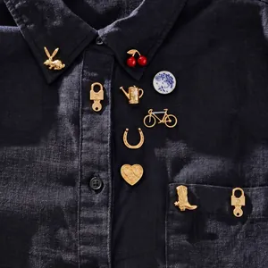 Détail de broches dorées vintage avec motifs cerise et lapin sur une chemise sombre.