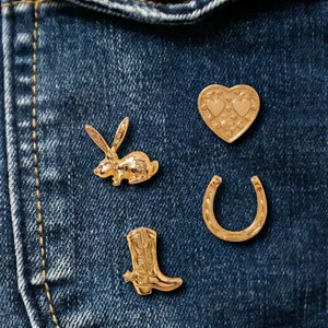 Vue détaillée de broches dorées rétro avec lapin et botte de cow-boy sur tissu en jean