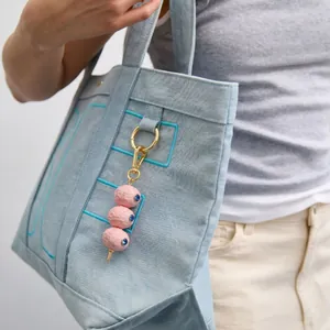 Detail eines rosa Perlen-Taschenanhängers mit Goldverschluss an Denim-Tasche