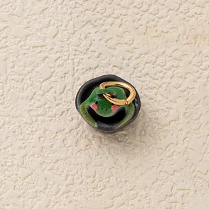 Close-up detail of a cute green frog charm in a black bowl with a golden hanging ring.