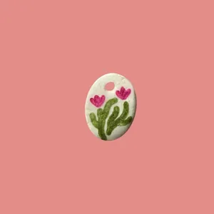 Detalle de un colgante ovalado blanco con motivos florale rosas pintados a mano.