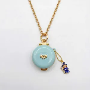 Detalle de collar guardapelo de esmalte azul claro con lazo dorado y dije de bruja