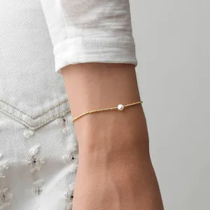 Gros plan d'un bracelet minimaliste doré orné d'une perle blanche sur le poignet