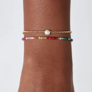 Gros plan d'un bracelet minimaliste en perles dorées avec perle et perles colorées.