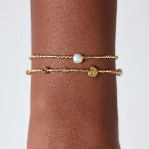 Gros plan de bracelets en perles dorées avec une perle blanche et un charm de coquillage.