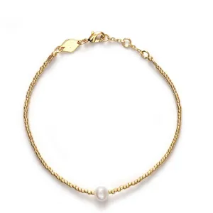 Vue détaillée d'un bracelet minimaliste en perles dorées avec une perle blanche