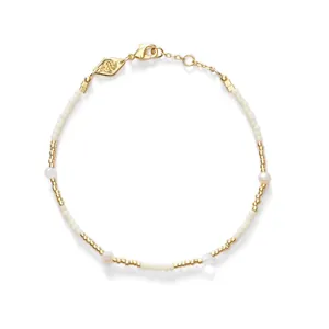 Gros plan d'un bracelet minimaliste en perles dorées avec perles de rocaille blanches et perles