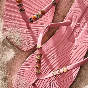 Gros plan de breloques de chaussures DIY émaillées sur tongs roses sur le sable