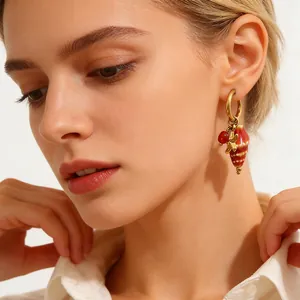 Close-up detail of stainless steel hoop earring with red bead and conch shell charm