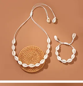 Set collana e bracciale con conchiglie di ciprea fatti a mano su uno sfondo intrecciato rustico.