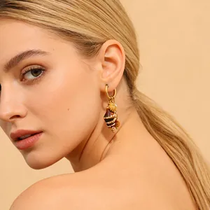 Close-up of gold stainless steel earring featuring a conch and shell pendant on a model