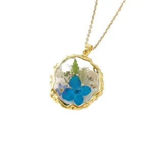 Elegant gold necklace with round resin pendant featuring preserved blue and white dried flowers.