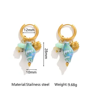 Detail view of oceanic conch and shell charms on gold stainless steel hoop earrings