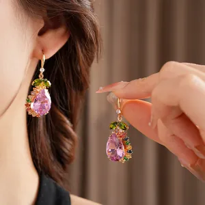 Close-up of elegant gold-toned pear-shaped earrings featuring pink and multicolor crystals.