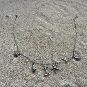 Hochwertige Edelstahl-Strandkette mit Meeresanhängern wie Seestern und Muscheln im Sand