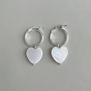 Close-up of elegant silver hoop earrings featuring white mother of pearl heart charms.