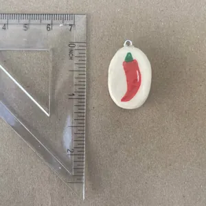 Detail view of hand-painted red chili pepper pendant with ruler for size reference