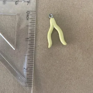 Pale yellow wishbone-shaped charm pendant shown with a ruler for size measurement detail
