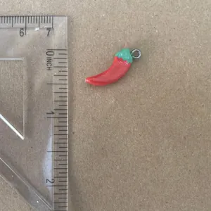 Close-up detail of a small red chili pepper pendant with ruler for size reference