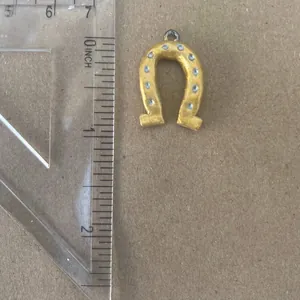 Close-up of a golden horseshoe charm pendant next to a ruler showing accurate size details